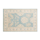 Traditional medium blue 4x6 Oushak area rug with muted ivory and beige floral medallions and a distressed cream border.
