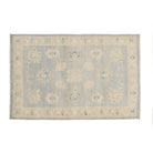 Traditional greyish blue 4x6 Oushak area rug with muted beige and ivory floral medallions, medium blue accents, and a distressed cream border.