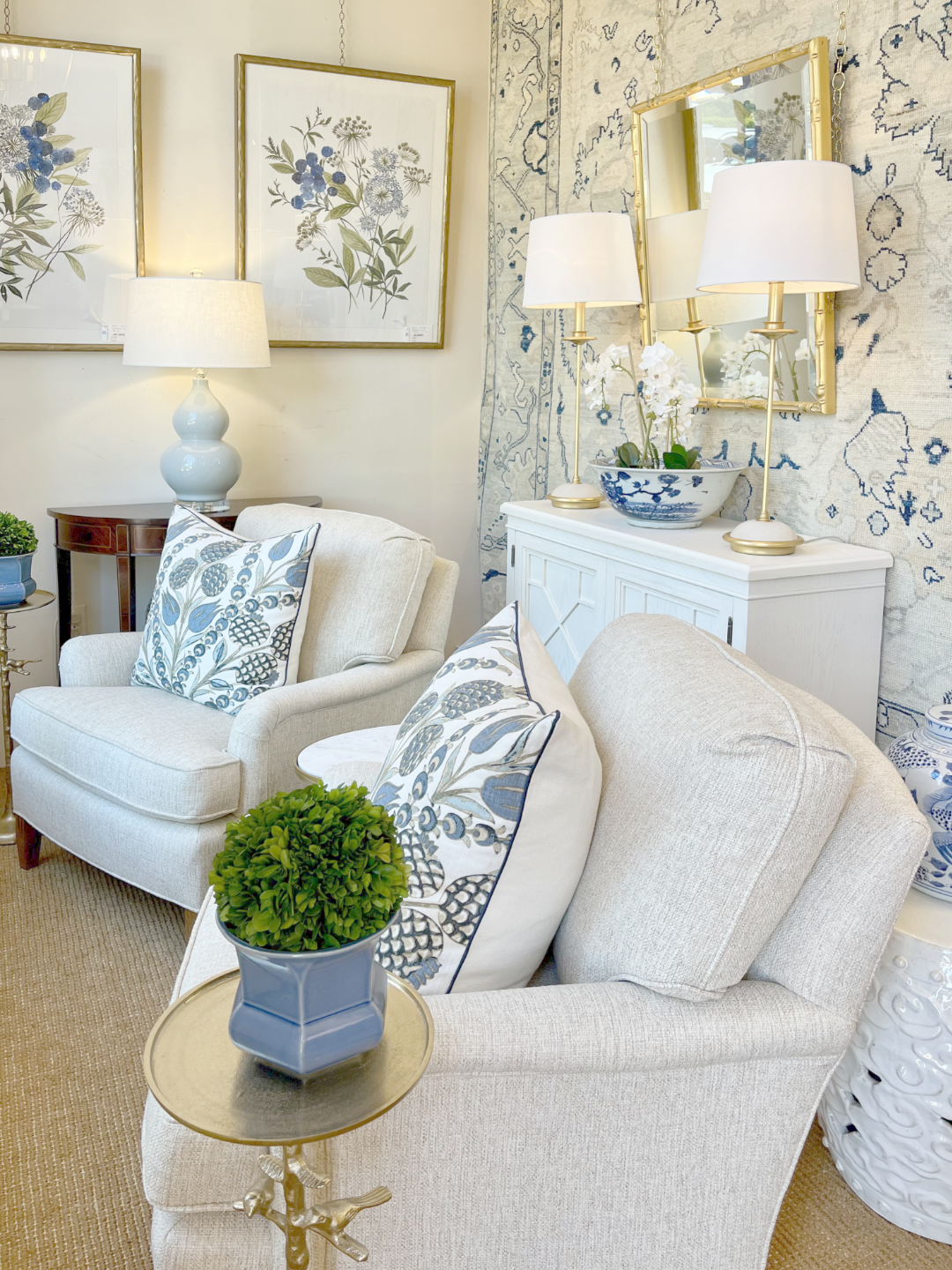 An ivory and navy Oushak area rug styled as a wall hanging backdrop in a bright living room with cream armchairs.