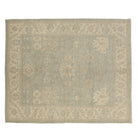 Muted mist blue 8x10 Oushak area rug with warm tan and cream floral motifs and a distressed border.